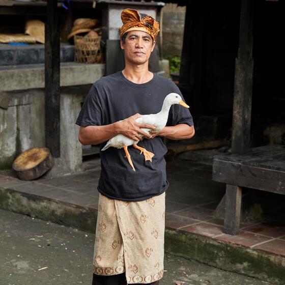 A Balinese man holding a duck outside a Paon