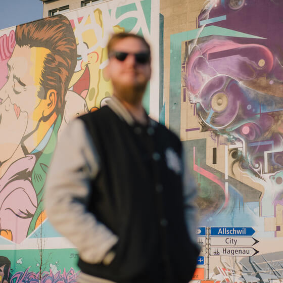 A man stands in front of some Basel street art