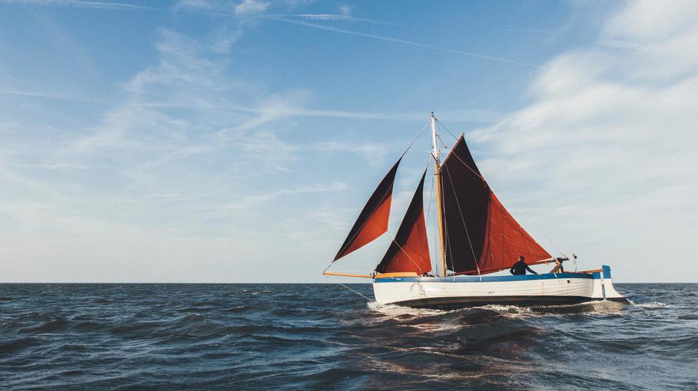 A red-sailed Norfolk Lugger sets out across the waves