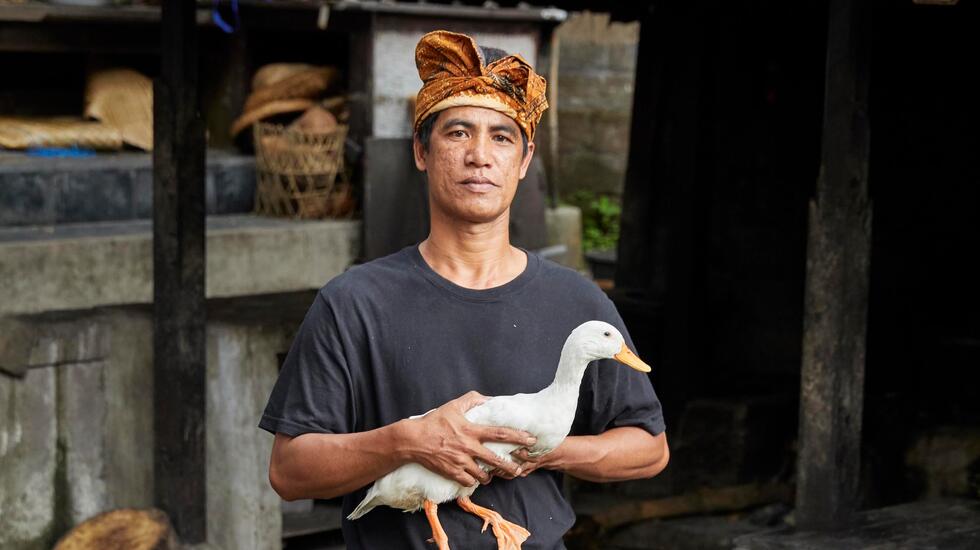 A Balinese man holding a duck outside a Paon