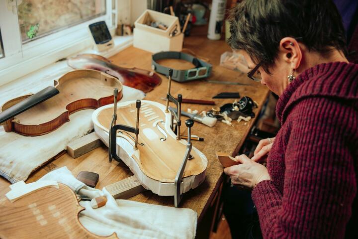 A woman bends over a violin she is restoring