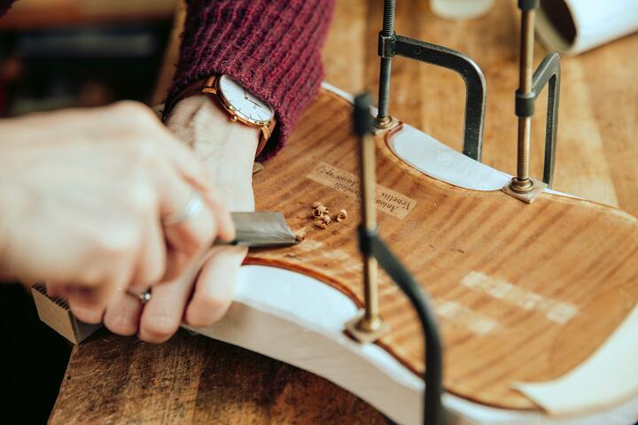 A woman chisels the wooden body of a violin