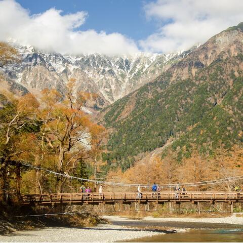 Walkers cross a bridge backdropped by snow-capped mountains