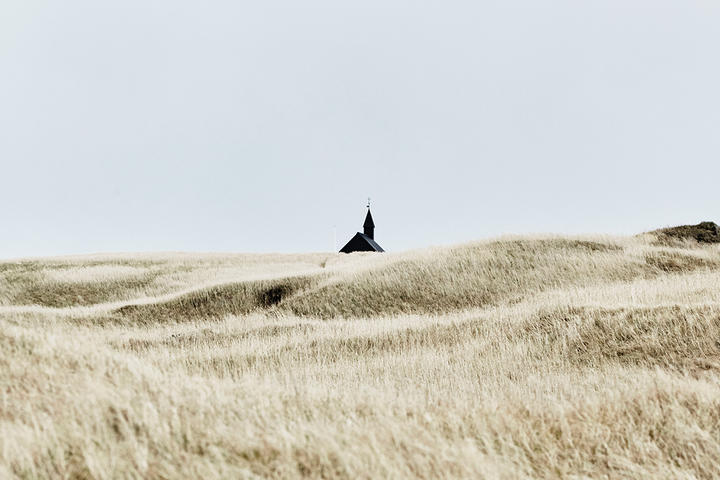 A black church against a blue sky and wheat field in Iceland